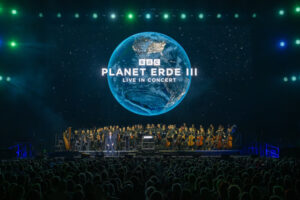 Auf der Leinwand ist das Logo Planet Erde II mit Weltkugel. Das Orchester steht mit dem Gesicht zum Publikum, die Rudolf Weber Arena in Oberhausen st sehr gut besucht