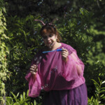 Eine Schauspielerin in einem pink lila Schmetterlingskostüm macht Seifenblasen